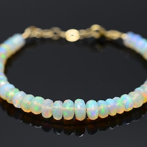 May include: A delicate bracelet featuring iridescent opal beads strung together with a gold chain and clasp. The opals display a range of colors, including white, blue, and hints of orange. The bracelet is approximately 7 inches in length.