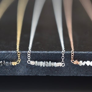 Puede incluir: Tres delicados collares con una fila de peque&ntilde;os diamantes en bruto engastados en un dise&ntilde;o simple de alambre. Los collares se muestran sobre una superficie negra y est&aacute;n disponibles en oro, plata y oro rosa.