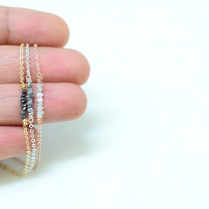 Puede incluir: Tres cadenas delicadas de oro con peque&ntilde;os diamantes en bruto. Las cadenas est&aacute;n superpuestas, la cadena superior con diamantes negros, la cadena del medio con diamantes grises y la cadena inferior con diamantes blancos.
