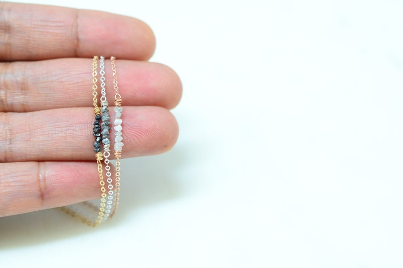 Puede incluir: Tres cadenas delicadas de oro con peque&ntilde;os diamantes en bruto. Las cadenas est&aacute;n superpuestas, la cadena superior con diamantes negros, la cadena del medio con diamantes grises y la cadena inferior con diamantes blancos.