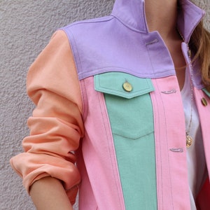 Puede incluir: Una chaqueta vaquera rosa, verde y naranja con un dise&ntilde;o de bloques de color contrastantes. La chaqueta tiene un estilo vaquero cl&aacute;sico con cierre de botones y bolsillos.