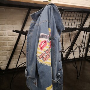 May include: A light blue denim jacket with a colorful graphic print on the left sleeve. The print features a red mouth, yellow stripes, and the text "NO BAD DAYS".