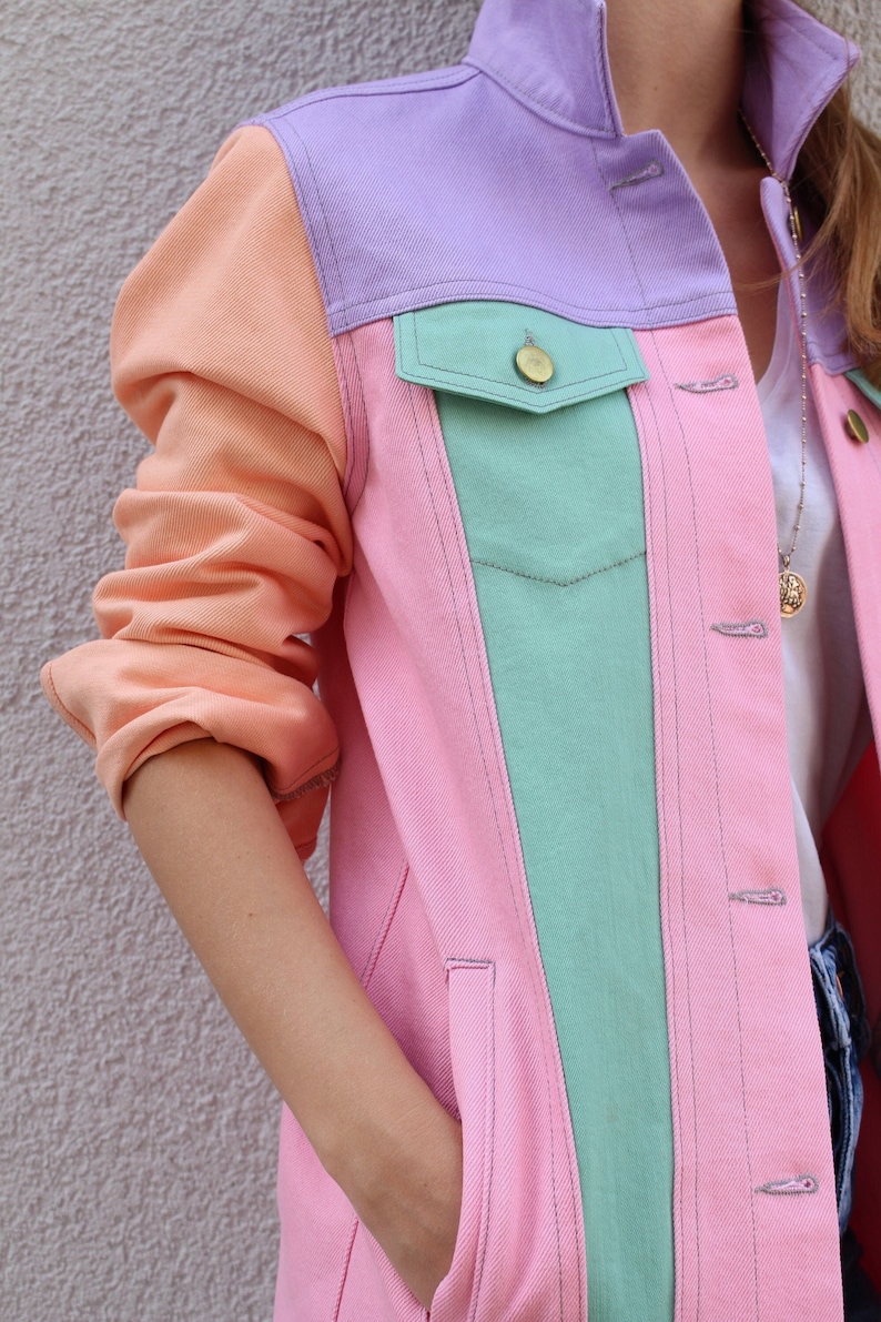 Puede incluir: Una chaqueta vaquera rosa, verde y naranja con un dise&ntilde;o de bloques de color contrastantes. La chaqueta tiene un estilo vaquero cl&aacute;sico con cierre de botones y bolsillos.