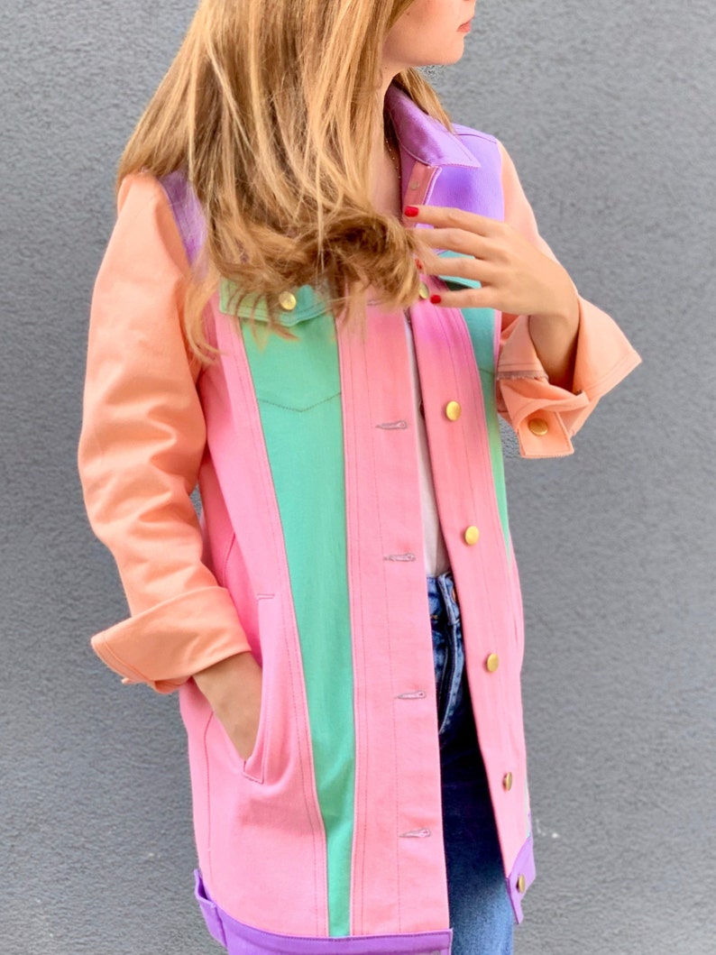 Puede incluir: Una chaqueta vaquera rosa con un dise&ntilde;o de bloques de color verde, morado y naranja. La chaqueta tiene cierre de botones y bolsillos.
