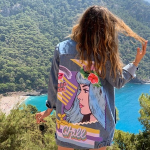 May include: A blue denim jacket with a colorful graphic design on the back. The design features a woman with blue hair, a flower crown, and the words "chill" and "bad days".