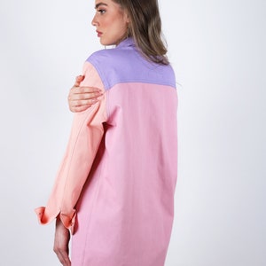 Puede incluir: Una camisa de manga larga con cuello y dise&ntilde;o de bloques de color. La camisa es rosa, melocot&oacute;n y lavanda. La camisa tiene cierre de botones y un bolsillo en el pecho izquierdo.