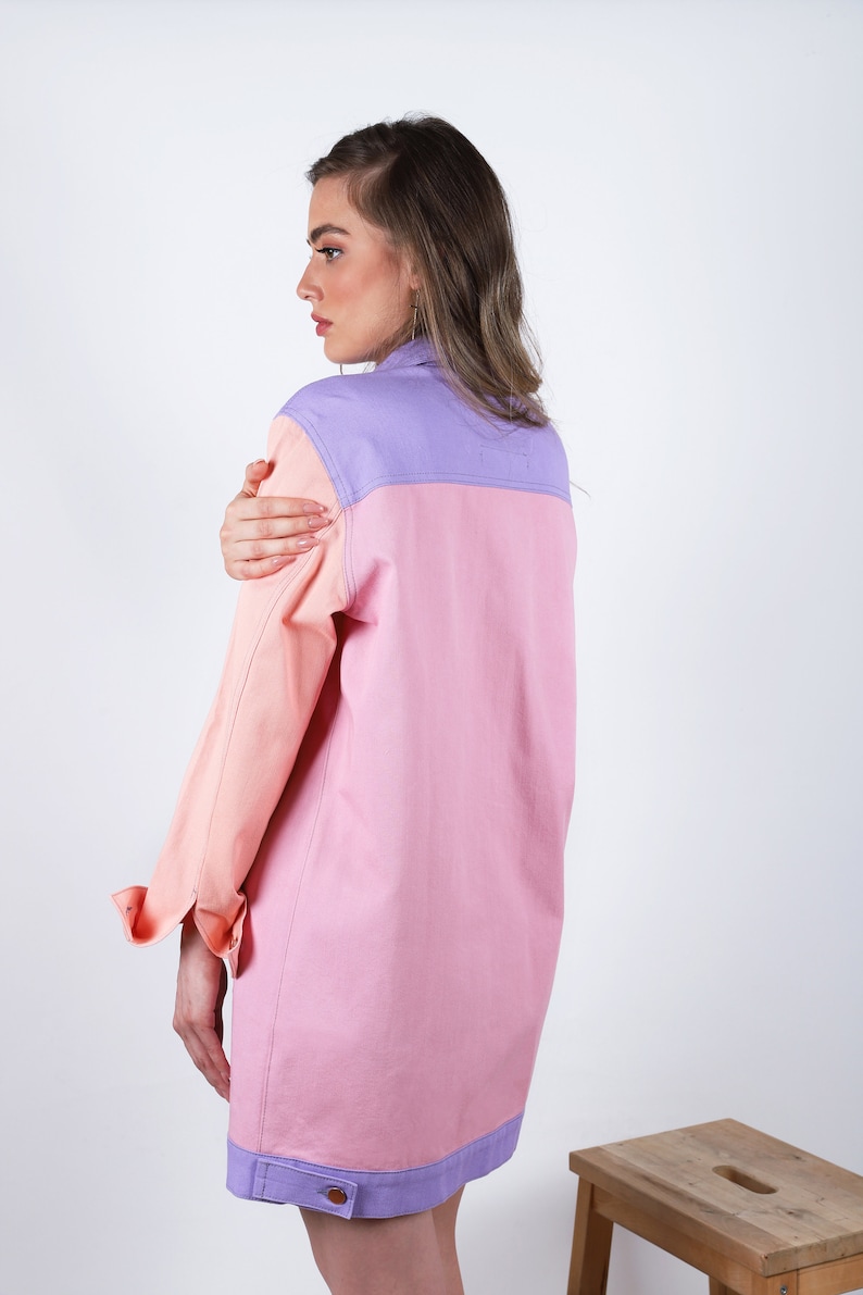 Puede incluir: Una camisa de manga larga con cuello y dise&ntilde;o de bloques de color. La camisa es rosa, melocot&oacute;n y lavanda. La camisa tiene cierre de botones y un bolsillo en el pecho izquierdo.