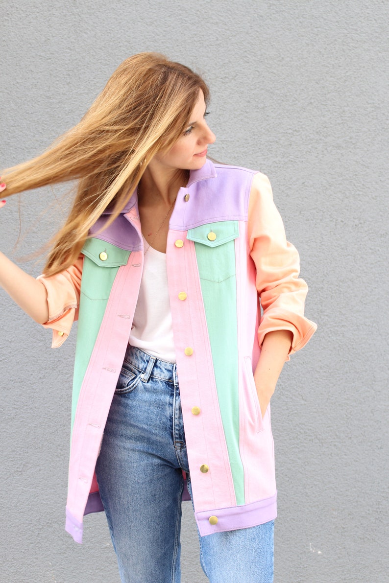 Puede incluir: Una chaqueta vaquera de color pastel con un esquema de color rosa claro, verde claro y lavanda. La chaqueta tiene botones dorados y un estilo cl&aacute;sico de chaqueta vaquera.