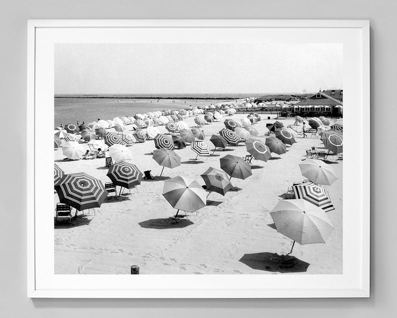 May include: A black and white photograph of a beach scene with many striped umbrellas and chairs. The umbrellas are arranged in rows on the sand, with the ocean in the background.