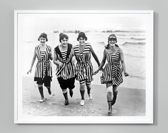 May include: Four women in black and white striped bathing suits run along a sandy beach. They are smiling and appear to be having fun.
