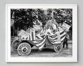 May include: Black and white photograph of a group of women in a car decorated with American flags. The women are holding signs that read "Votes for Us - When Women Vote We Are Women".