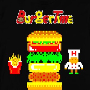 Könnte beinhalten: Schwarzes T-Shirt mit einem Pixelbild eines Burgers, Pommes und eines Kochs. Der Text "BurgerTime" befindet sich über dem Burger.