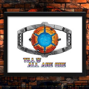 May include: Framed artwork featuring a stylized eye design with a central blue orb, surrounded by orange and silver elements. The text "TILL ALL ARE ONE" is below the eye, with a Transformers logo. The artwork is in a black frame.