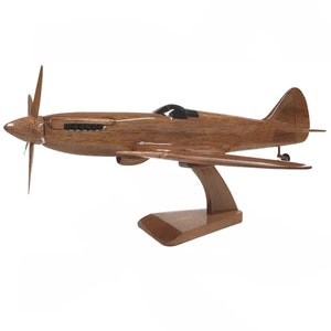 Può includere: Un modello in legno di un aereo vintage con un'elica e un supporto. Il modello è dipinto in una finitura in legno naturale.