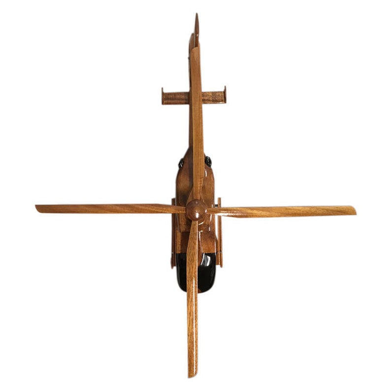 May include: A wooden model of a helicopter with brown wood and black accents. The helicopter has a single rotor and a tail rotor. The model is viewed from above.