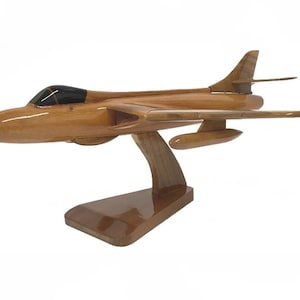 Può includere: Un modello in legno di un aereo da caccia a reazione con una finitura marrone. L'aereo è montato su un supporto in legno.