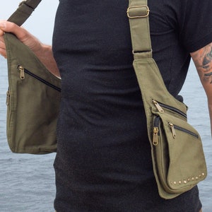 May include: Olive green shoulder bag with multiple zippered pockets and adjustable straps. The bag has a vertical design and is worn across the chest. The bag has brass-colored hardware and is made of a durable canvas material.