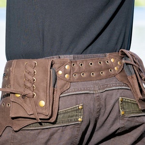 Puede incluir: Un cinturón de cuero marrón con múltiples bolsillos y un detalle de encaje. El cinturón tiene ojales y botones metálicos.