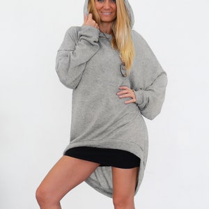 May include: A grey oversized hoodie with a long, asymmetrical hemline. The hoodie has a drawstring hood and a relaxed fit.
