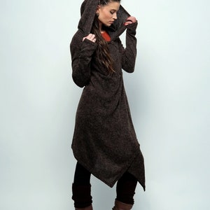 Peut inclure: Une robe pull à capuche marron avec une longue ligne d'ourlet asymétrique. La robe est faite d'un tissu doux et tricoté et a une coupe décontractée. Le mannequin porte des bottes marron.