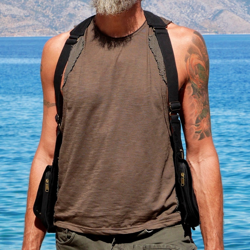 May include: A person wearing a brown tank top with a black crossbody bag with two zippered pockets. The bag is worn over one shoulder and has a strap that goes across the chest.