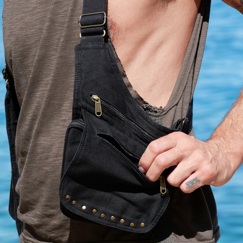May include: A black canvas crossbody bag with multiple pockets and a zipper closure. The bag has gold-colored studs around the bottom edge.