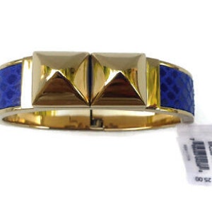 May include: A gold bangle bracelet with blue patterned leather accents and two gold pyramid-shaped studs.