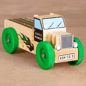 May include: A wooden toy truck with green wheels, black flames, and the text "ASH&CO POWER" and "ASH CO 3" printed on the sides.
