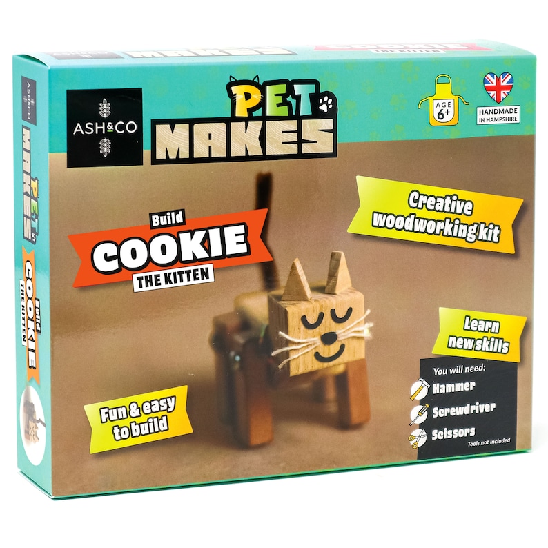 May include: A wooden craft kit to build a cat named Cookie. The box features a photo of the finished project, a cat with brown and white fur. The box is green and brown with the words "Pet Makes" and "Build Cookie the Kitten".