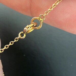 May include: Close-up of a gold necklace clasp and chain. The chain is delicate, with small links. The clasp is a simple design, with a small loop for attaching the necklace. The necklace has small turquoise and white beads.
