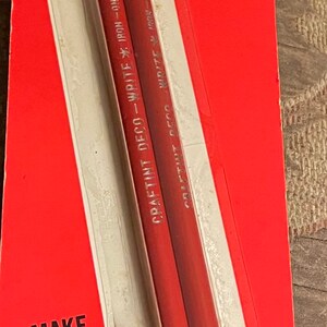 May include: Vintage Craftint Deco-Write iron-on transfer pencils in original packaging. The red pencils are labeled "DECO-WRITE IRON-ON TRANSFER PENCILS" and are packaged on a red and white card. The packaging reads "MAKE YOUR OWN STAMPED GOODS."
