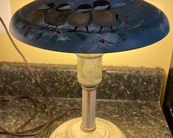 May include: A vintage table lamp with a blue metal shade featuring a painted scene of birds on a branch. The base is green with a painted bird on a branch.