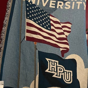Puede incluir: Una manta tejida con el texto "HIGH POINT UNIVERSITY" en blanco. El diseño incluye una bandera estadounidense y una bandera con las letras "HPU". La parte inferior de la manta dice "EXTRAORDINARY EDUCATION | INSPIRING ENVIRONMENT | CARING PEOPLE".