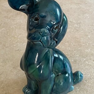 May include: A ceramic figurine of a dog sitting with its head tilted. The dog is a deep teal blue color with a glossy finish.