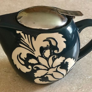 May include: A blue ceramic teapot with a white floral design and a silver lid. The teapot has a handle and a spout.