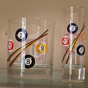 May include: Two clear glass cups with a billiard ball design. The larger cup has a design of billiard balls with numbers 2, 9, 11, and 8. The smaller cup has a design of billiard balls with numbers 2, 9, 11, and 8.