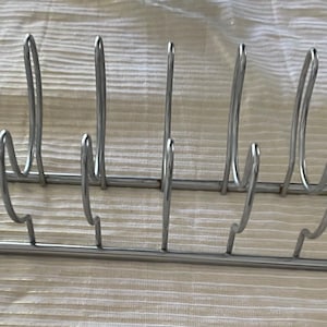 May include: A silver-colored metal dish rack with multiple vertical dividers and curved supports. The rack is designed to hold plates or dishes upright for drying. The design is simple and functional, suitable for kitchen use.