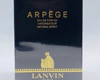 Può includere: Una scatola nera con lettere dorate per un flacone di profumo Lanvin Arpege. La scatola presenta il nome del marchio Lanvin Paris e il nome del prodotto Arpege Eau de Parfum Vaporisateur Natural Spray. La scatola include anche il volume del profumo, 100 ml, e l'equivalente in once liquide, 3,3 fl oz.