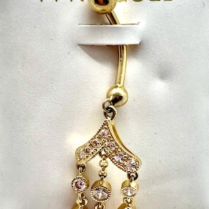 May include: 14KT gold belly button ring with a dangling charm. The charm is shaped like a teardrop and has a row of small clear stones around the edge. The ring is on a white card with the words "14 KT GOLD" printed on it.