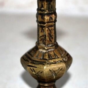 Puede incluir: Un candelero de latón antiguo con base y parte superior en forma de estrella. El candelero tiene un diseño detallado y ornamentado con patrones grabados y una pátina oscura, mostrando su edad y artesanía.