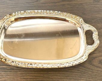 Puede incluir: Una bandeja plateada rectangular con asas ornamentadas y un borde decorativo. La bandeja tiene una superficie pulida y reflectante, ideal para servir alimentos o exhibir objetos. Las asas son curvas y añaden elegancia al diseño.