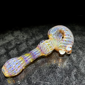 May include: A colorful glass pipe with a swirling pattern of yellow, purple, and blue. The pipe has a rounded bowl and a long, slender stem. The glass is translucent, allowing light to pass through.
