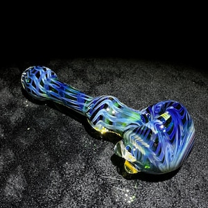 May include: A glass pipe with a blue, green, and white swirl design. The pipe is made of thick glass and has a rounded bowl.