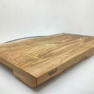 Op de afbeelding: Een groot, rechthoekig houten snijplank met een natuurlijke houtkleur en een licht ongelijke rand. De plank heeft aan alle kanten een verhoogde rand en wordt ondersteund door twee kleine voetjes. De plank is gebrandmerkt met de tekst "Rollins" in zwart.