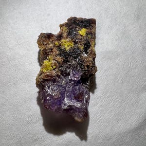 Può includere: Una roccia viola e marrone con cristalli gialli. La roccia ha una superficie ruvida e irregolare.