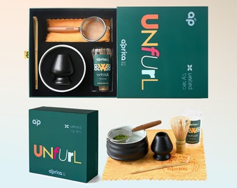 May include: A matcha tea set with a dark green box that reads "UNFURL" in colorful letters. The set includes a whisk, a bowl, a scoop, a sifter, and a whisk holder. The brand name "aprika" is visible on the box and accessories.