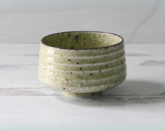 May include: A green ceramic tea bowl with a speckled glaze and a textured, ridged exterior.