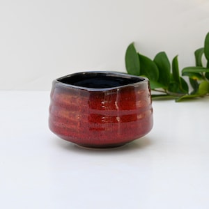 Könnte beinhalten: Eine rote und schwarze Teetasse aus Keramik mit einem strukturierten, wellenförmigen Design. Die Tasse ist aus Keramik und hat eine dunkle Glasur.