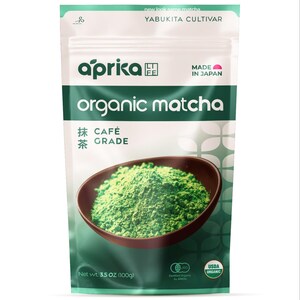 Puede incluir: Un paquete de t&eacute; matcha org&aacute;nico Aprica. El envase es blanco y verde con las palabras "organic matcha" en letras grandes. Se muestra un cuenco de polvo de matcha verde. El paquete contiene 100g de matcha.