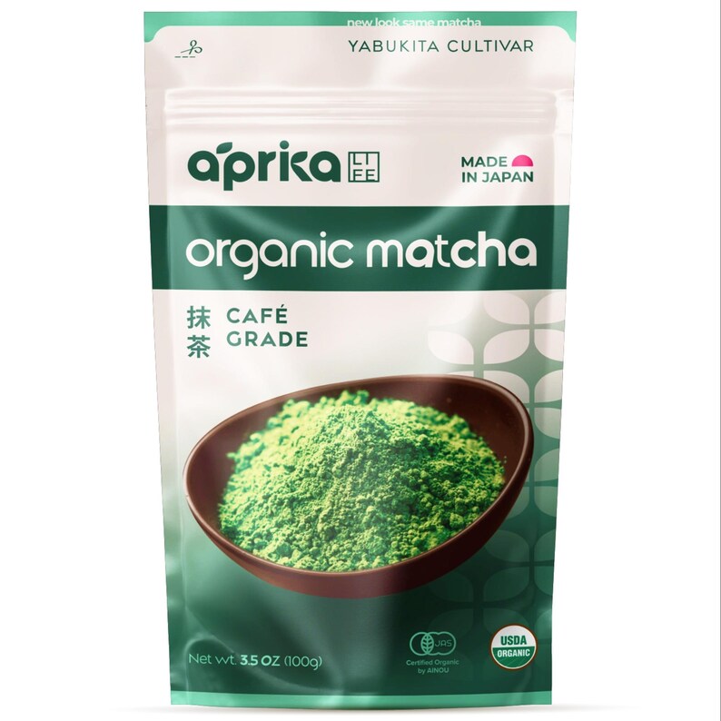 Puede incluir: Un paquete de t&eacute; matcha org&aacute;nico Aprica. El envase es blanco y verde con las palabras "organic matcha" en letras grandes. Se muestra un cuenco de polvo de matcha verde. El paquete contiene 100g de matcha.